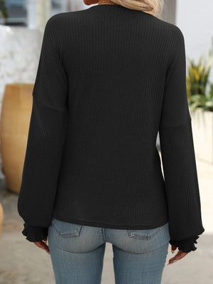 Black ribbed knit blouse with ruffled cuffs and long sleeves.