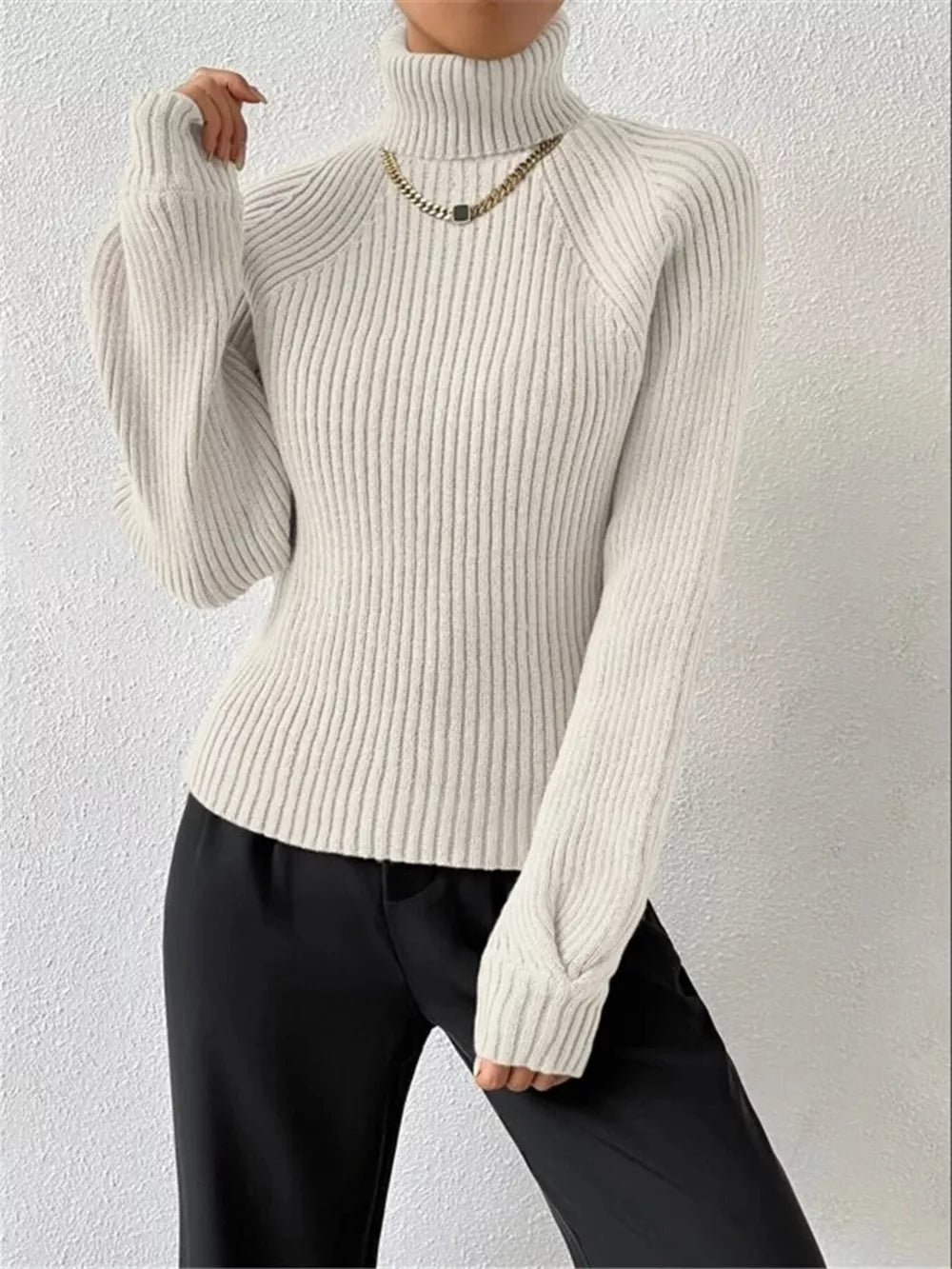 White ribbed turtleneck sweater with long sleeves and a gold chain necklace.