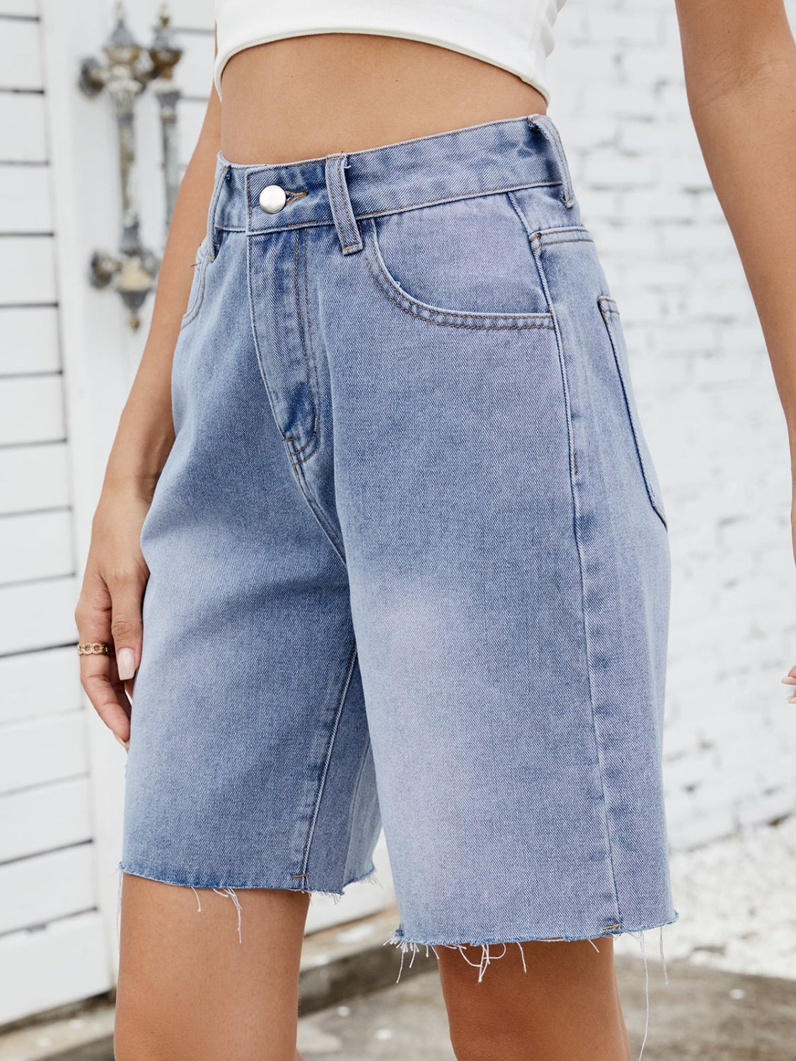 Longline denim cutoff shorts in medium wash with a raw hem.