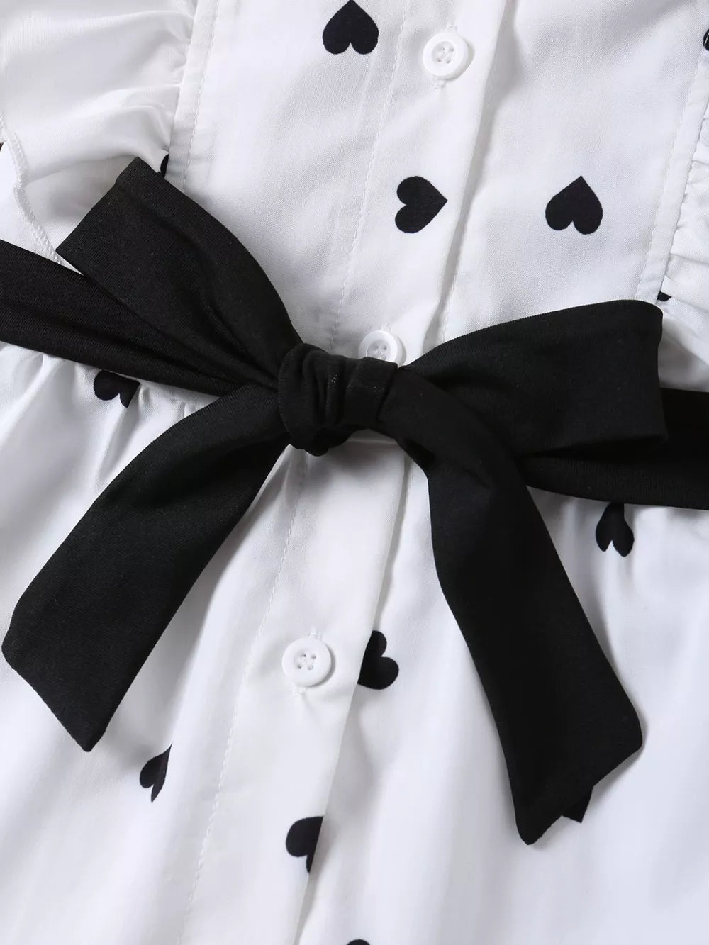 White toddler outfit with black heart print, button-down front, and black bow detail.
