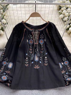 Black tie neck blouse with billowy sleeves and colorful floral embroidery.