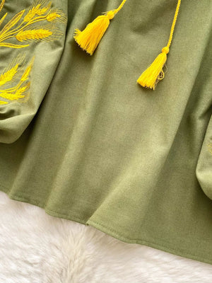 Green embroidered tie-neck folk blouse with yellow tassels and wheat detail on sleeve.