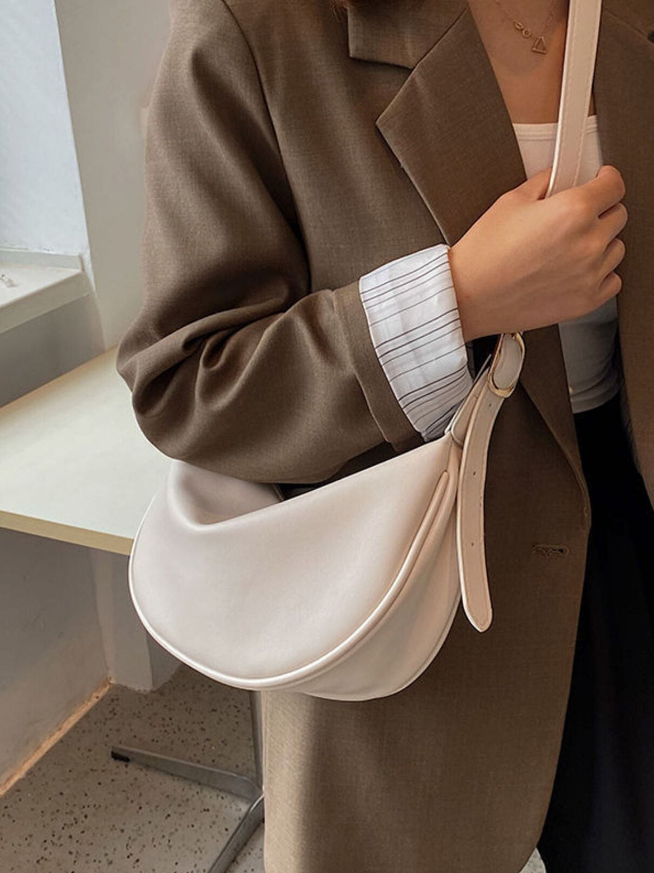 Crescent crossbody bag in beige white faux leather with adjustable strap.