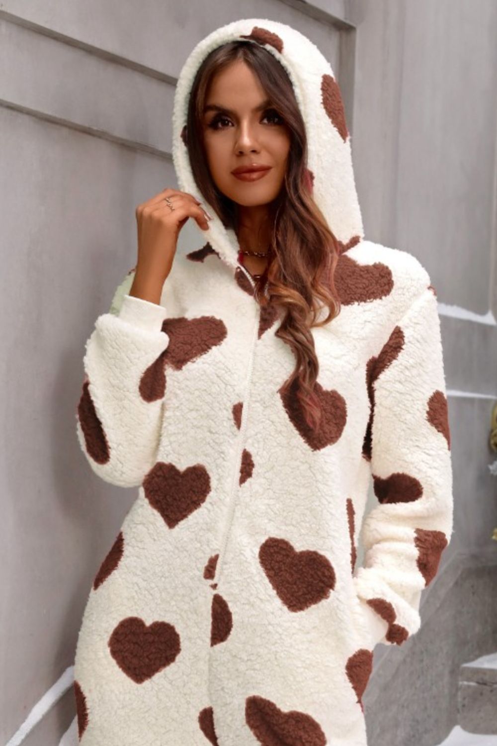 Cream sherpa onesie with brown hearts, hood, and long sleeves.