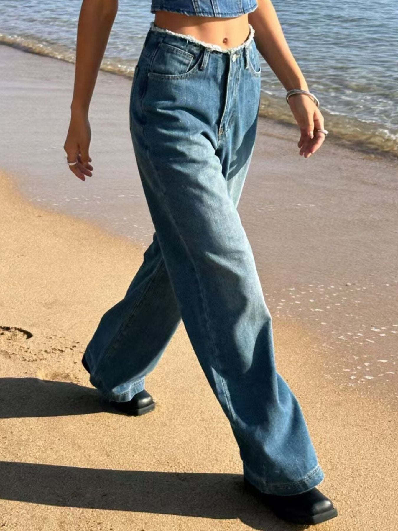 Blue denim maternity jeans with frayed hem and wide legs on a beach.