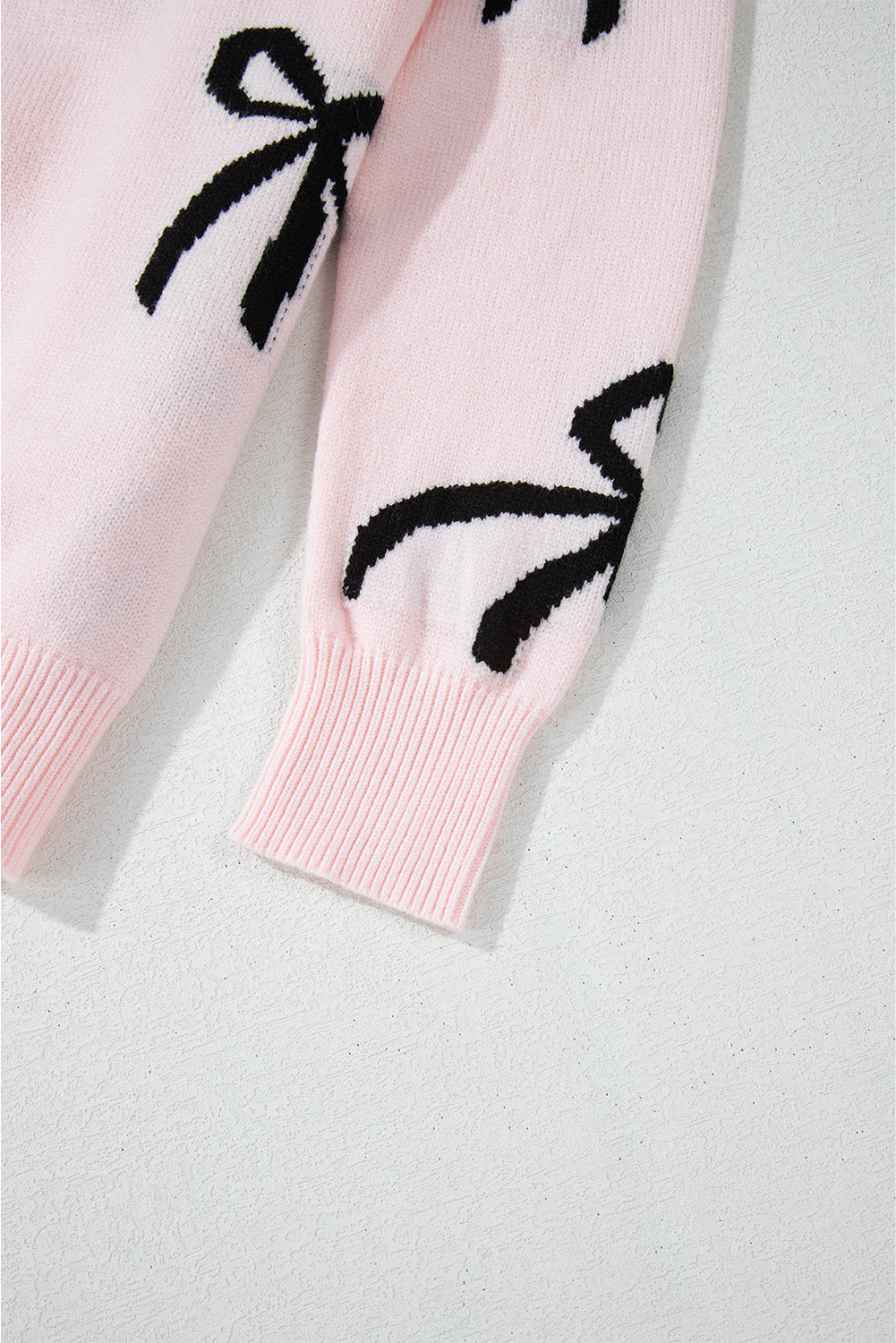 Blush pink knit crewneck sweater with black bow motifs and ribbed cuffs.