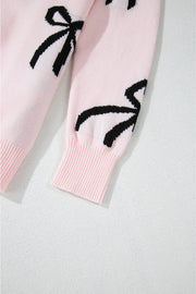 Blush pink knit crewneck sweater with black bow motifs and ribbed cuffs.