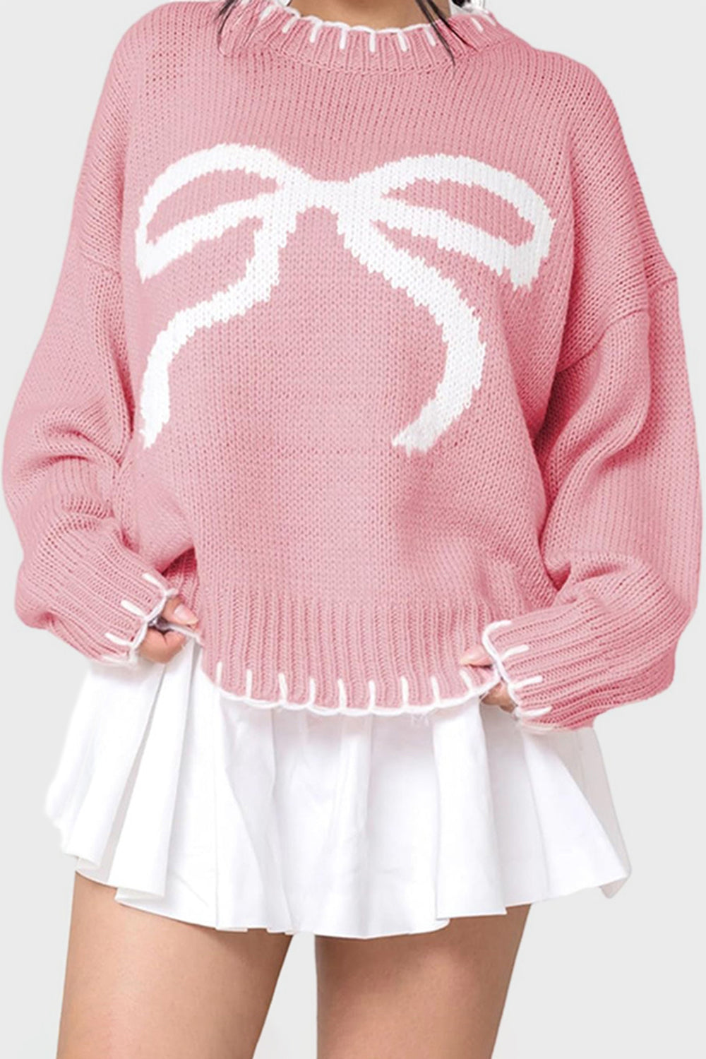 Graphic bow knit crewneck sweater in blush pink with white contrast stitching.