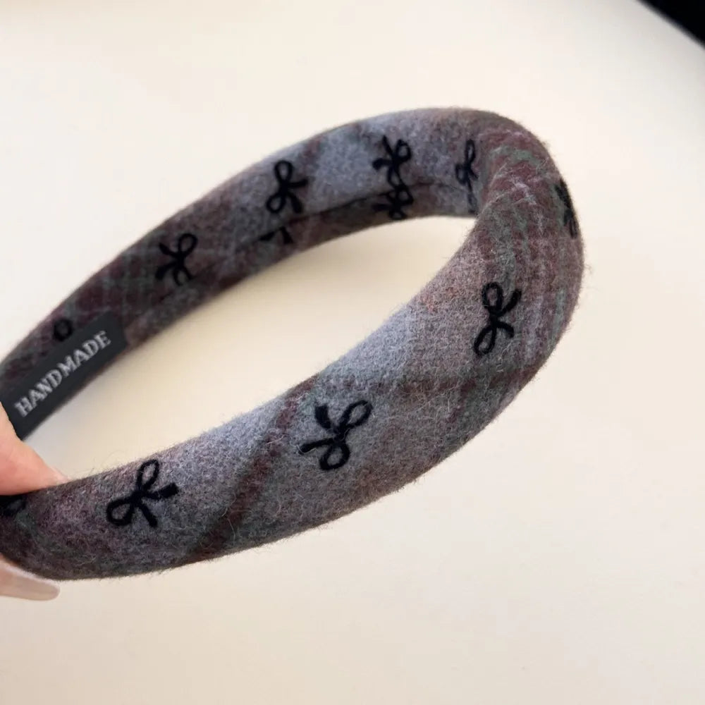Embroidered plaid padded headband in dark gray with black bow pattern.