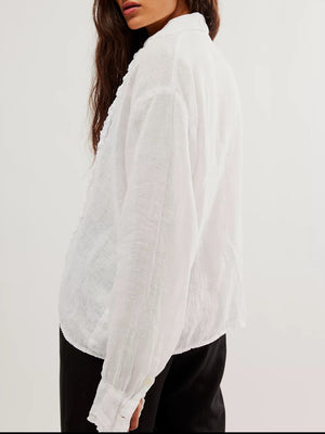 White linen button-down blouse with ruffled front detail and button cuffs.