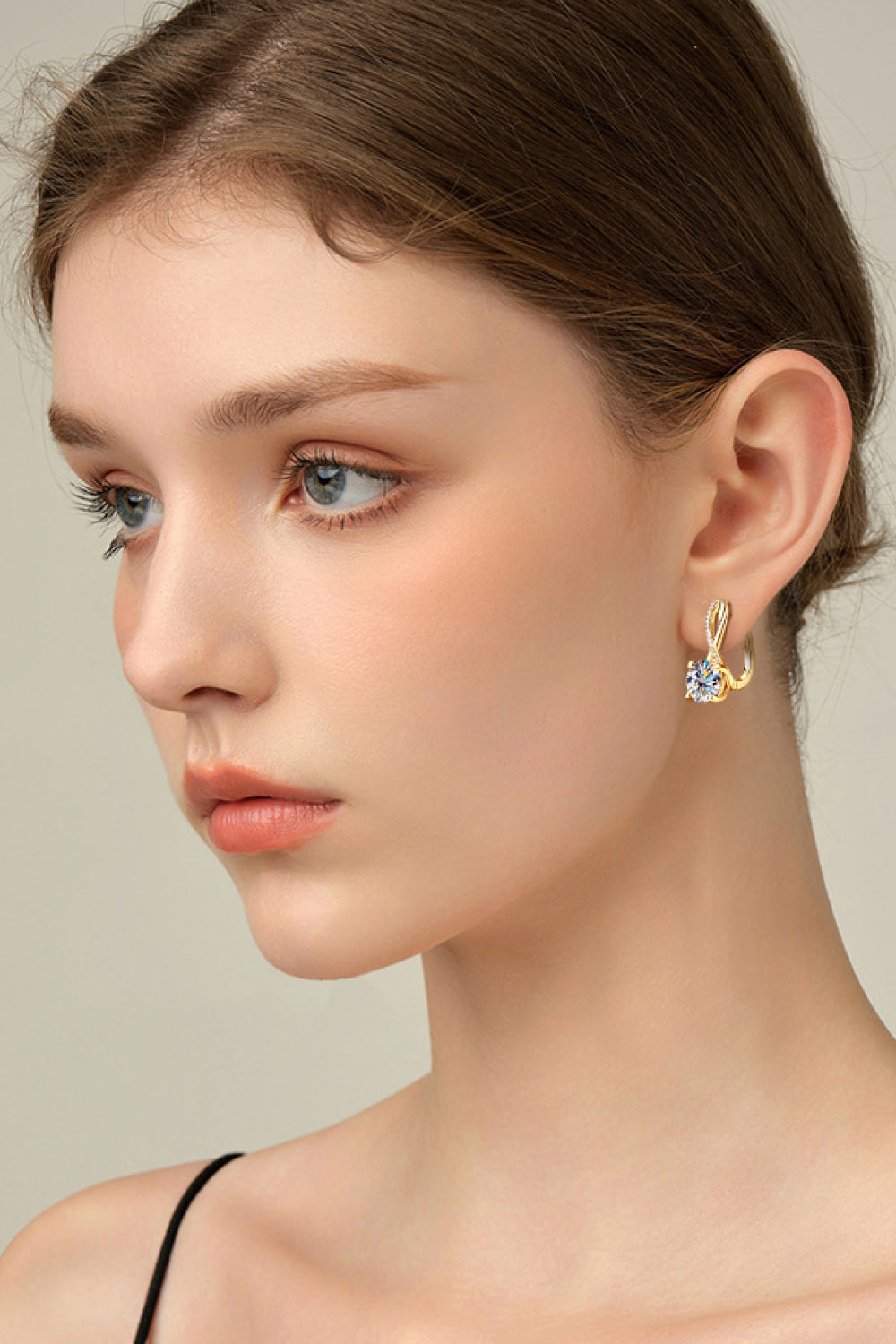 Gold crossover moissanite huggie earrings with a single round-cut stone.
