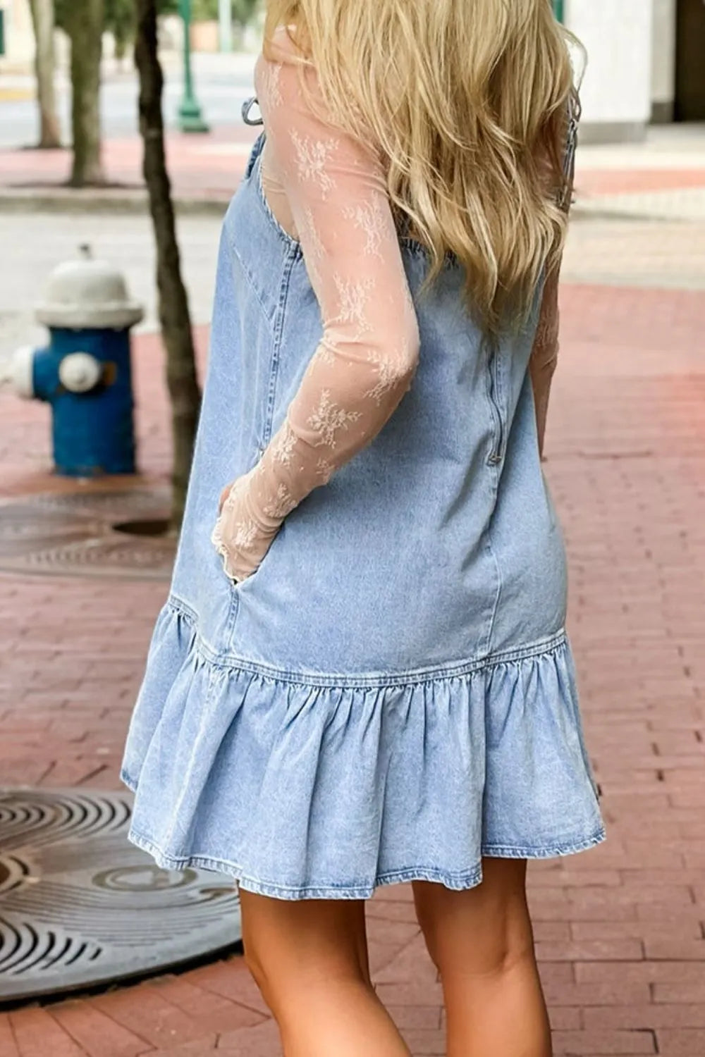 Light blue denim sundress with ruffled hem and pockets, styled with sheer lace sleeves.