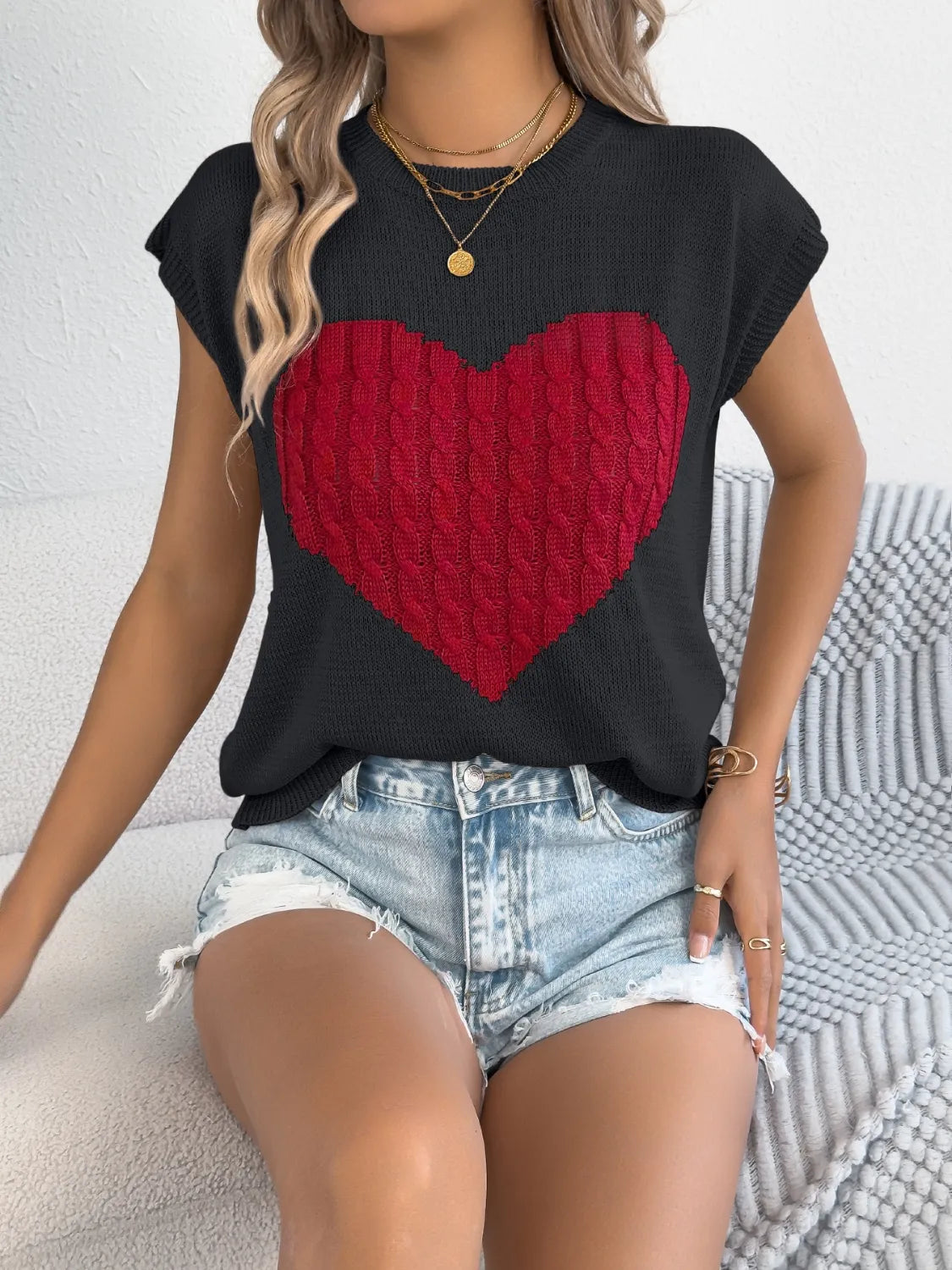 Black cable knit sweater vest with red cable knit heart graphic detail.