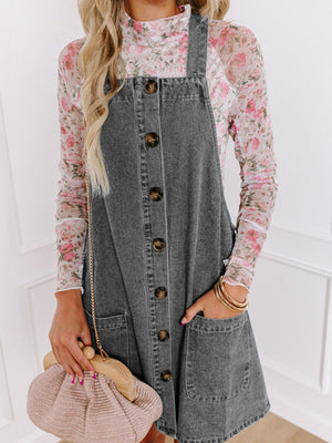 Faded gray denim pinafore dress with button front, pockets, and a floral top.