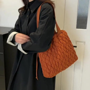 Terracotta quilted drawstring carryall bag with diamond pattern and leather strap.