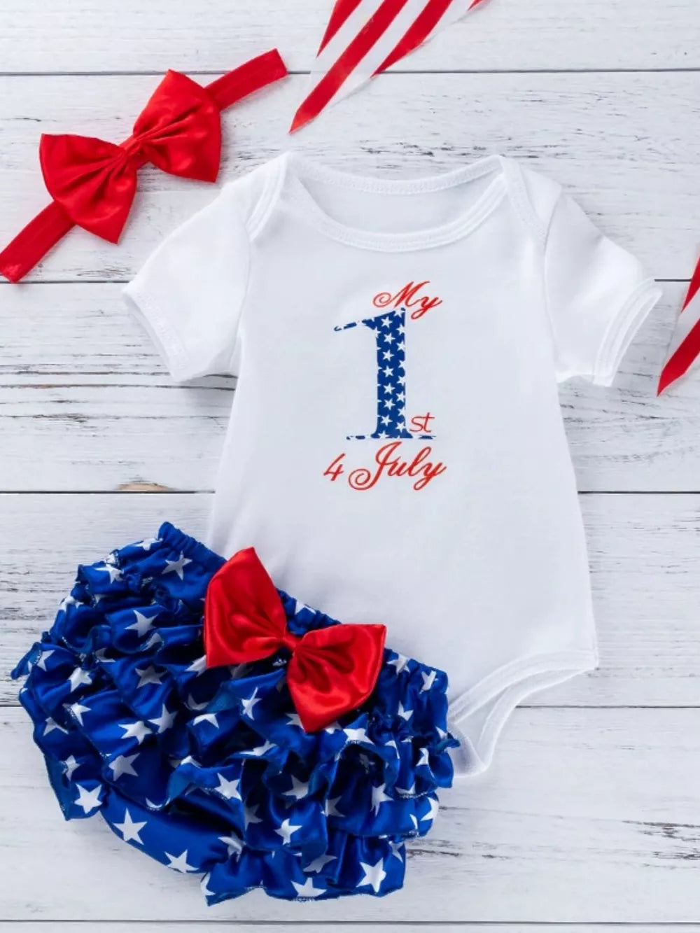 White baby onesie with "My 1st July" graphic and ruffled bloomer with stars and red bow.