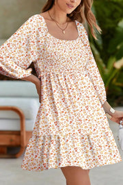Floral smocked mini dress with square neckline and tiered skirt in beige with orange and yellow floral print.