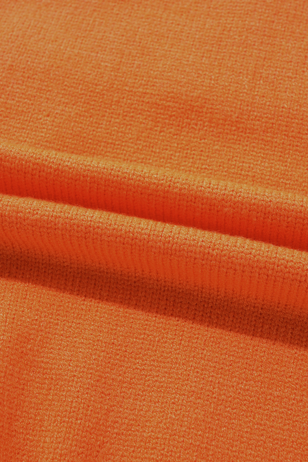 Orange knit sweater fabric detail with textured weave and soft folds.
