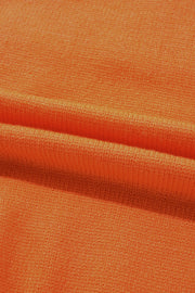 Orange knit sweater fabric detail with textured weave and soft folds.