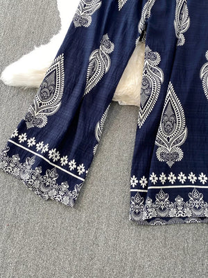 Navy blue wide leg romper with white paisley print and floral trim details.