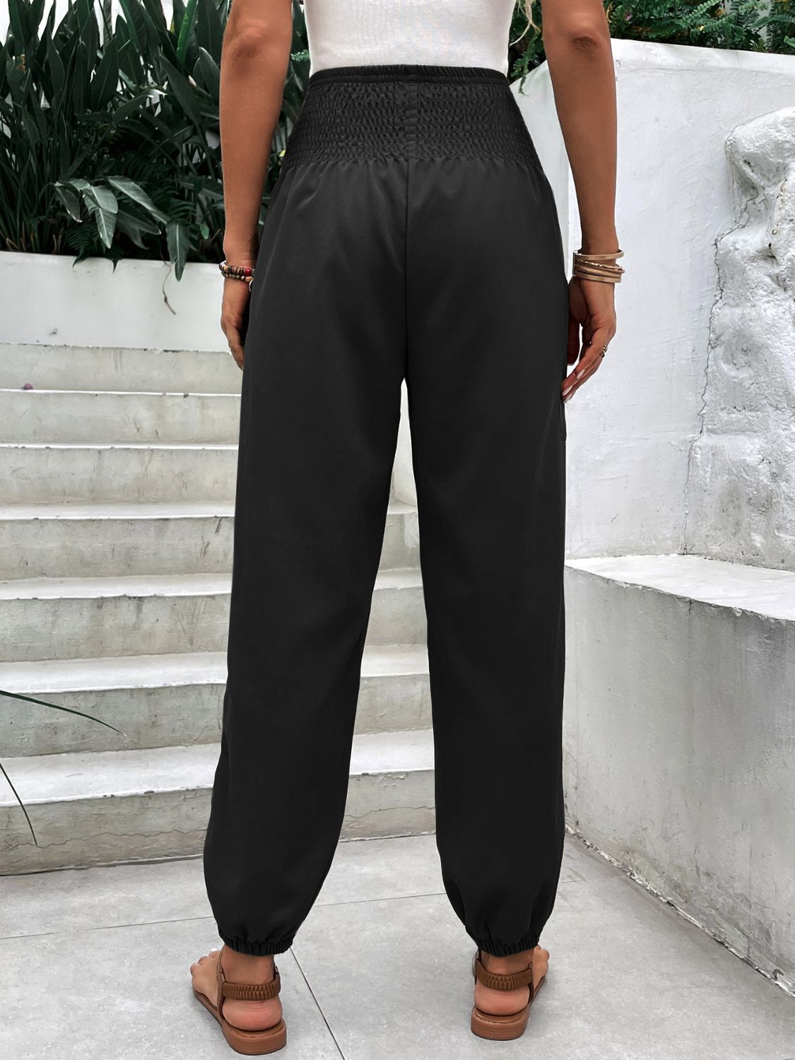 Black relaxed-fit trousers with smocked waistline and cuffed ankles.
