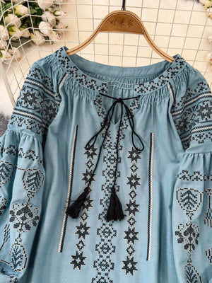 Light blue embroidered tie neck blouse with tassels and bell sleeves.
