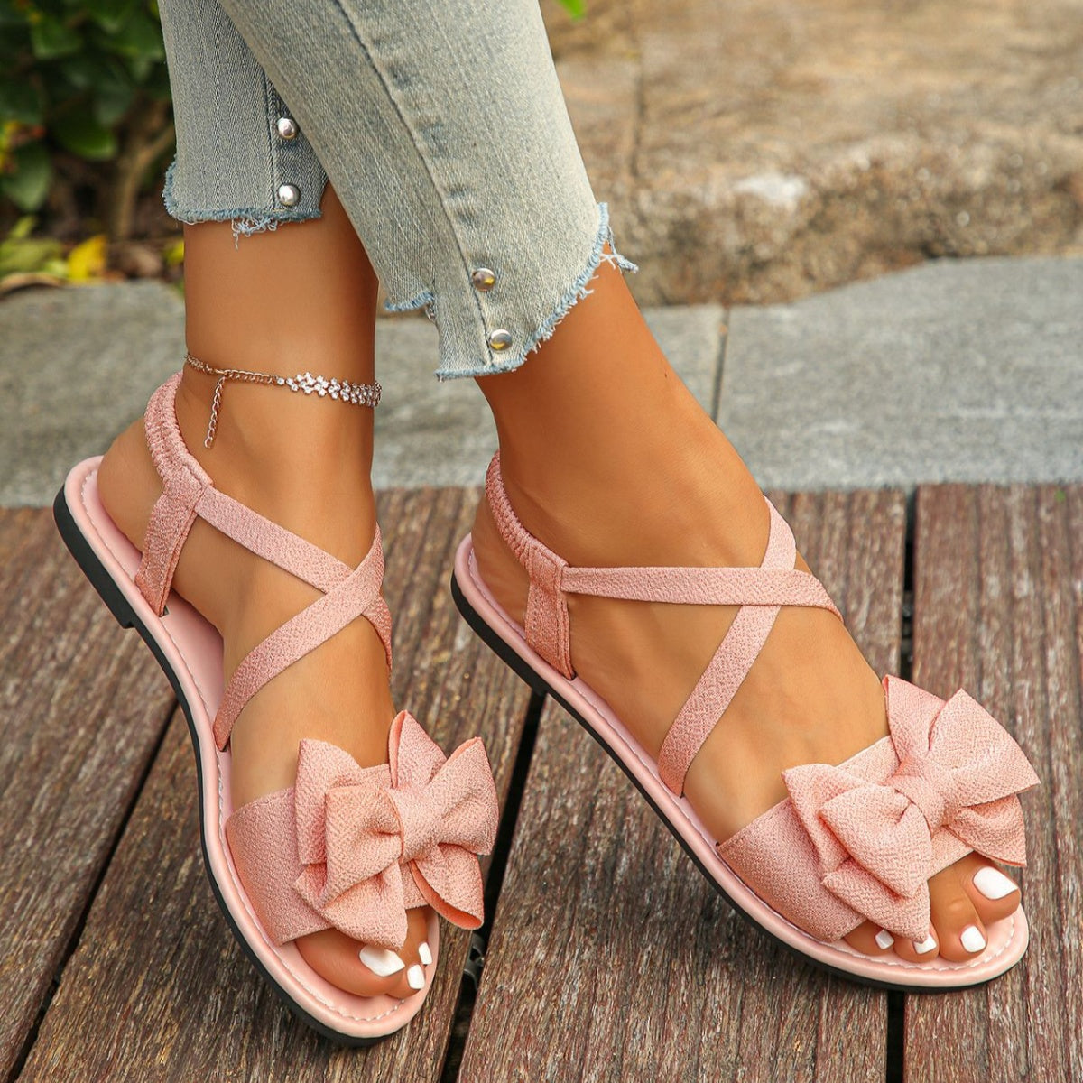 Pink crisscross bow sandals with ankle straps and a flat sole.