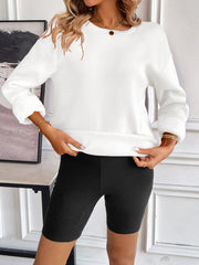 White relaxed fit sweatshirt with crewneck and cuffed sleeves, styled with black biker shorts.