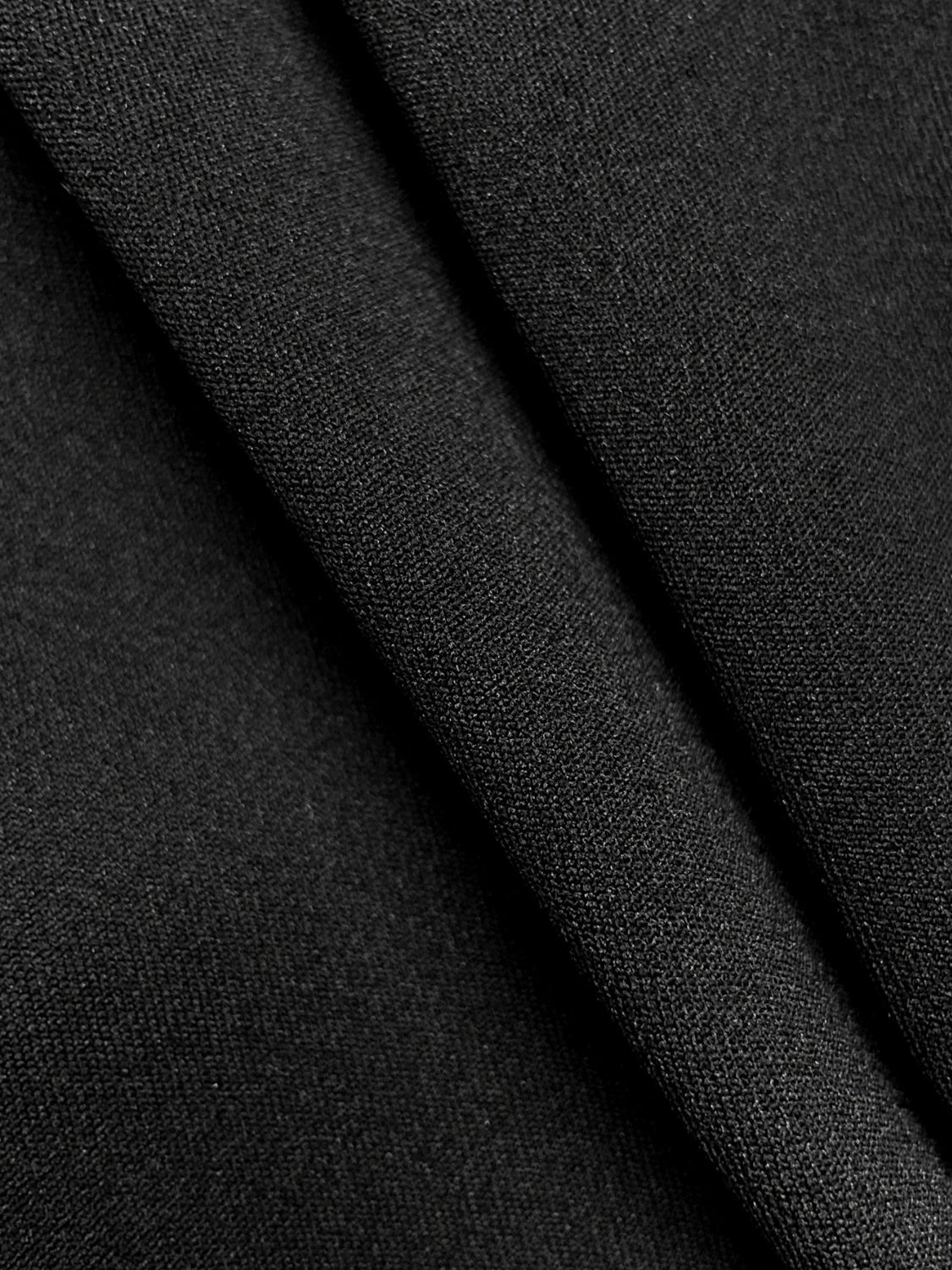 Black knit fabric detail of a drape-front blazer with sculpted silhouette.