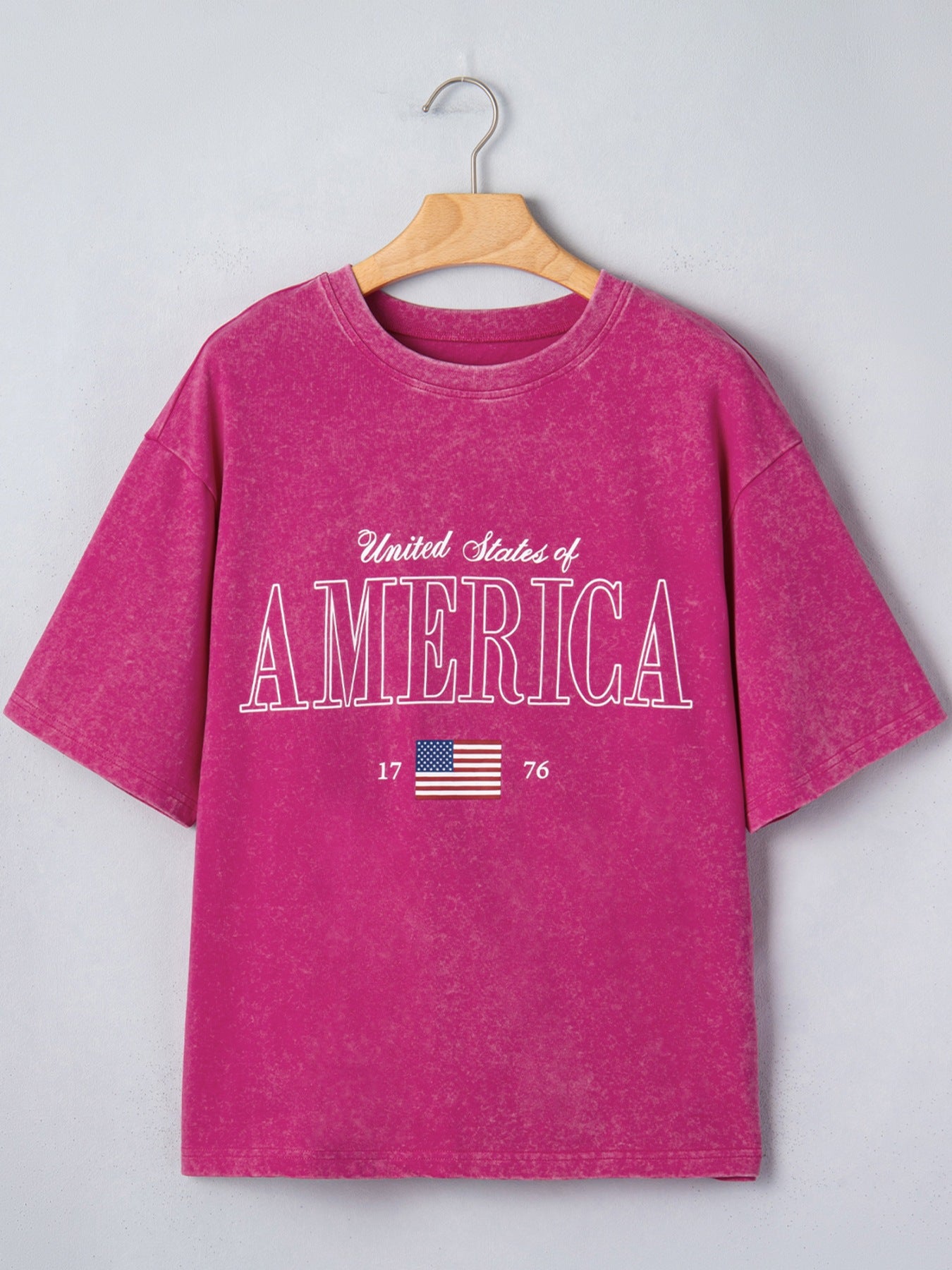 Patriotic graphic cotton t-shirt in magenta with "United States of America" text and US flag graphic.
