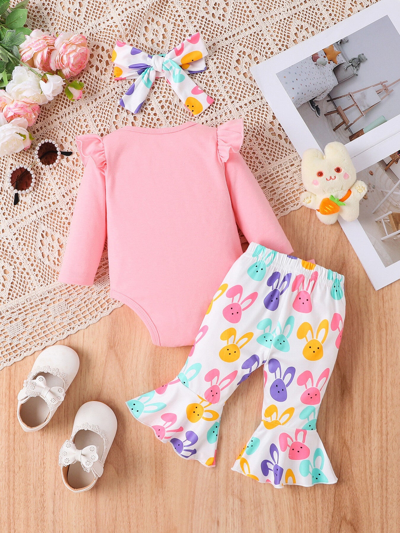Pink baby bodysuit with ruffled sleeves and bell-bottom pants with colorful bunny print.