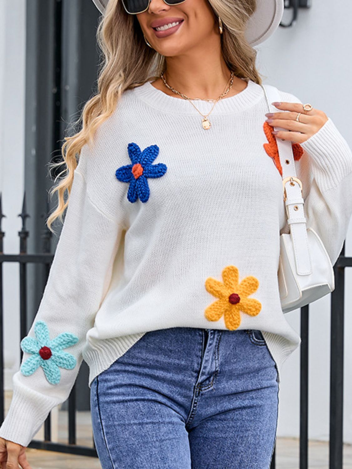White knit sweater with embroidered flower appliqués in blue, orange, yellow, and teal.