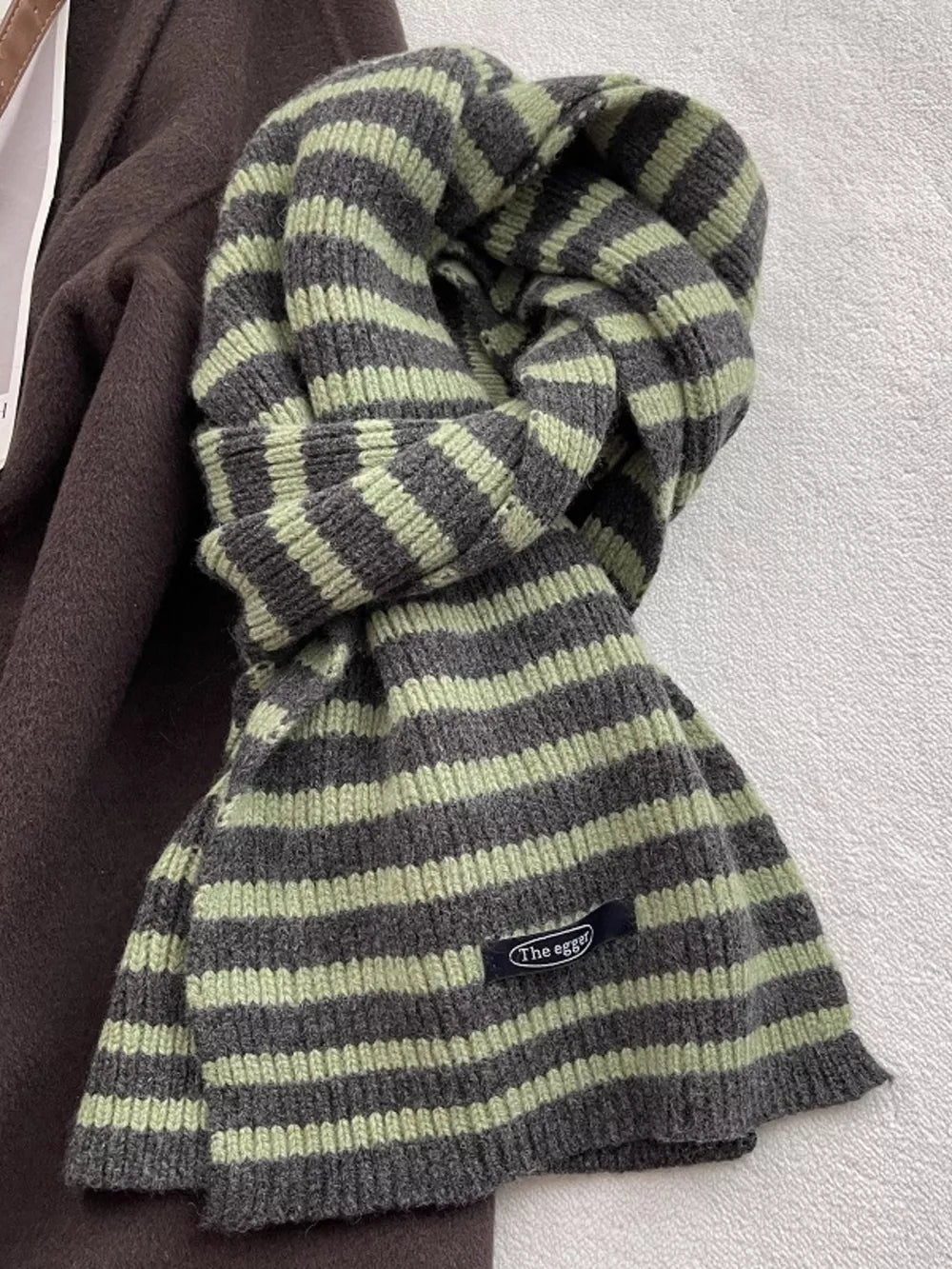 Cozy striped wool scarf in matcha green and grey with a small black tag.
