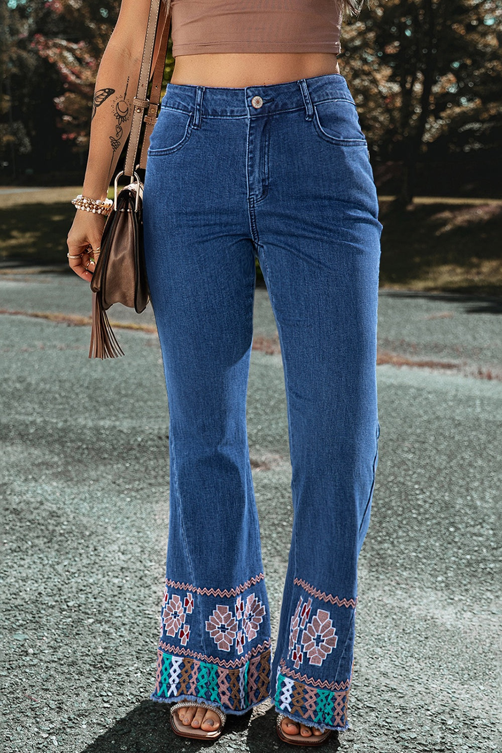 Embroidered hem flare jeans in medium blue denim with a boho pattern on the flared leg openings.