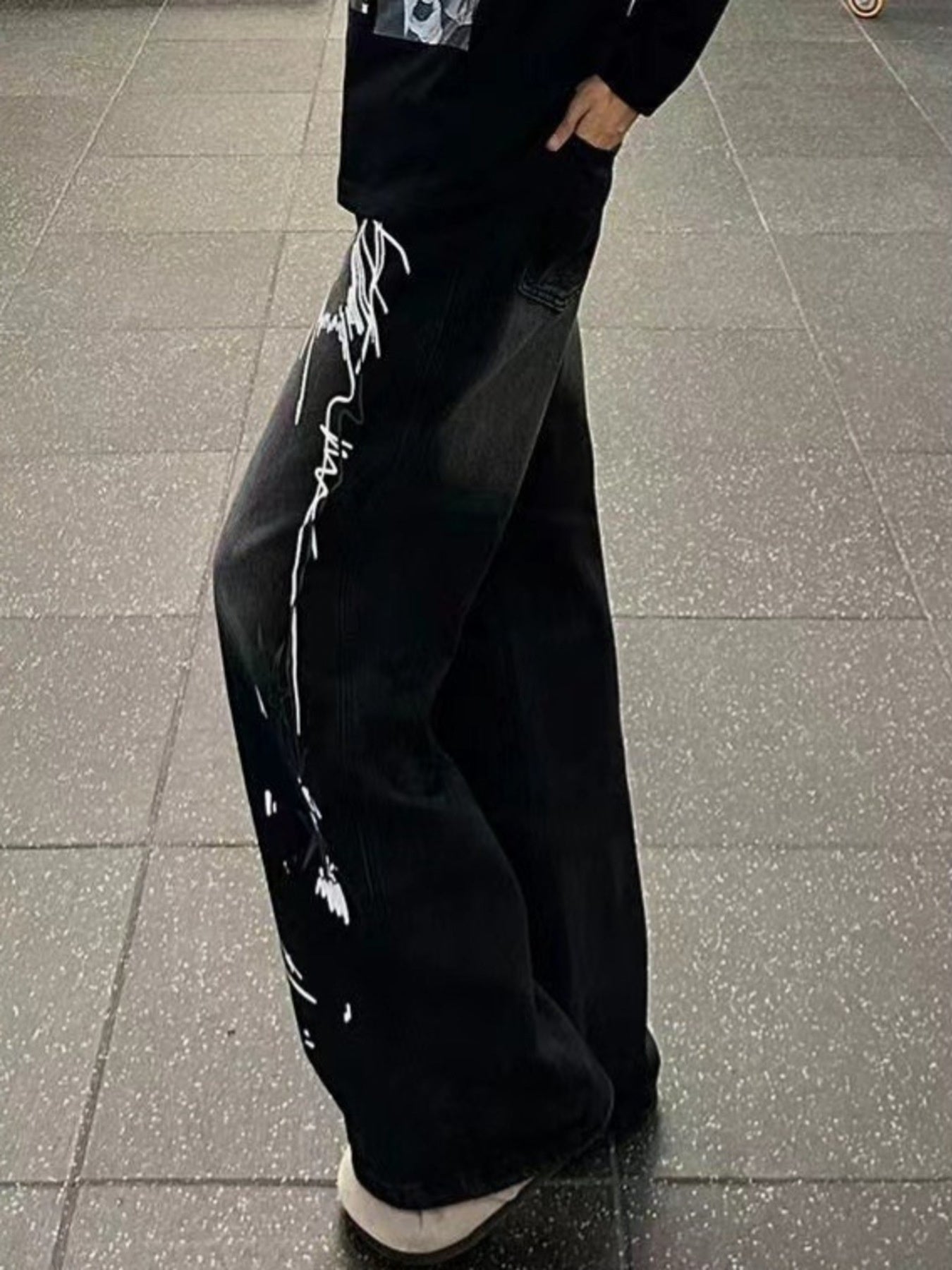 Men's black wide-leg jeans with white graffiti-style embellishments on the side.