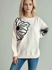 Cream knit sweater with black floral applique detail on chest and sleeve.