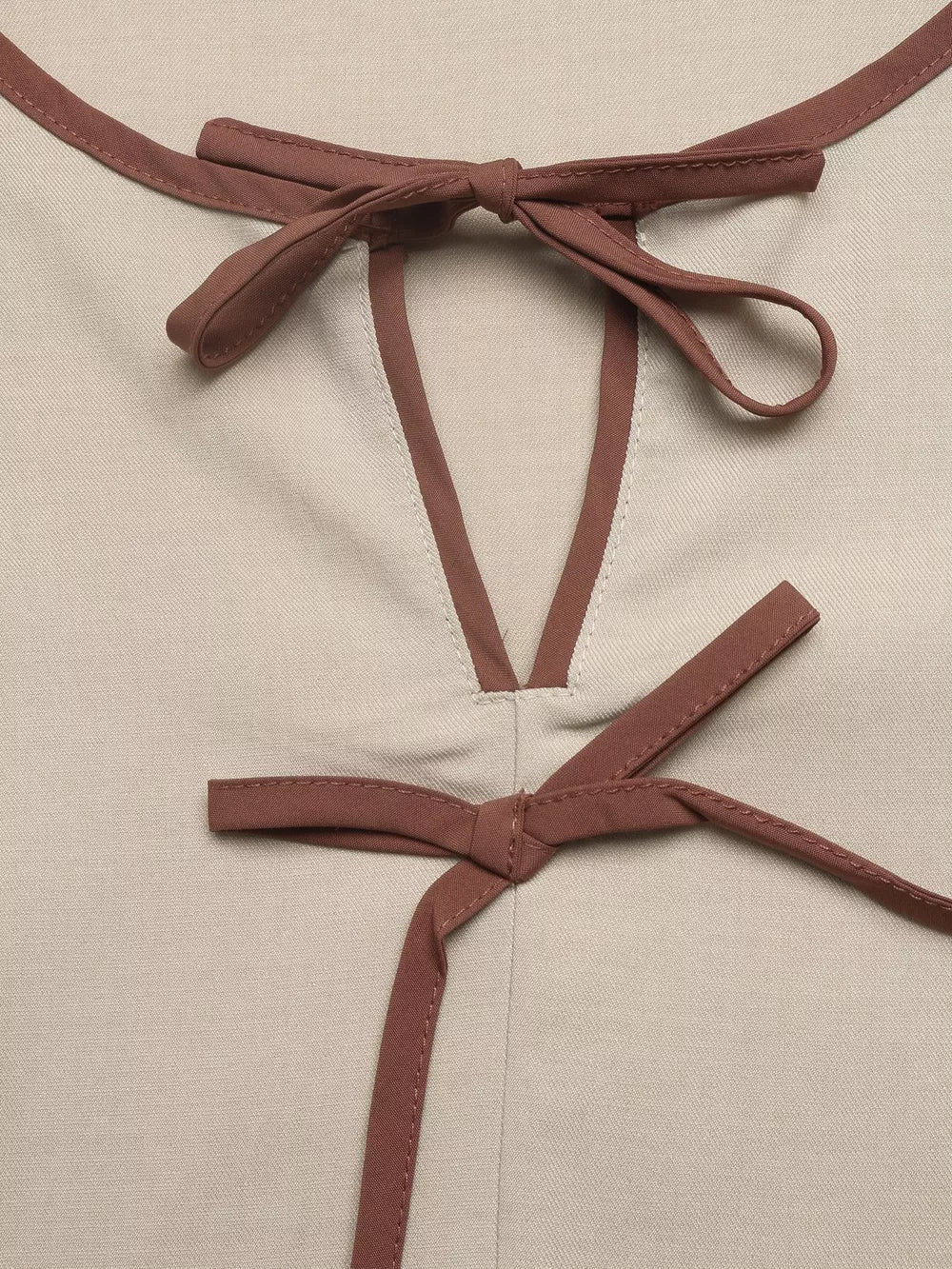 Charming V-neck blouse in beige with brown trim and bow details at neckline and waist.
