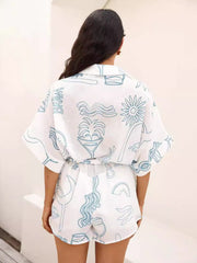White linen romper with cocktail print, tie waist, and short sleeves.