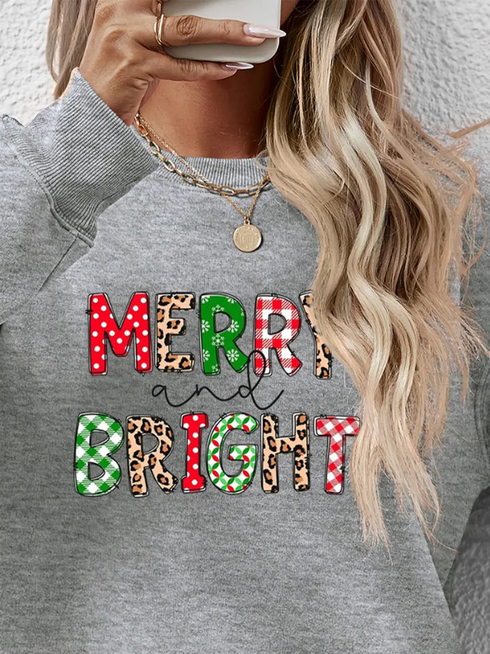 Gray crewneck sweatshirt with "Merry and Bright" graphic in festive patterns like buffalo plaid and leopard print.