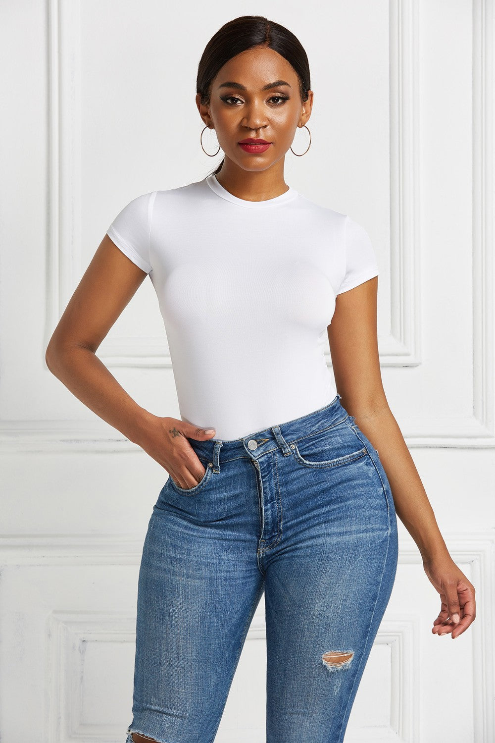 White crew neck bodysuit with short sleeves, styled with blue jeans.