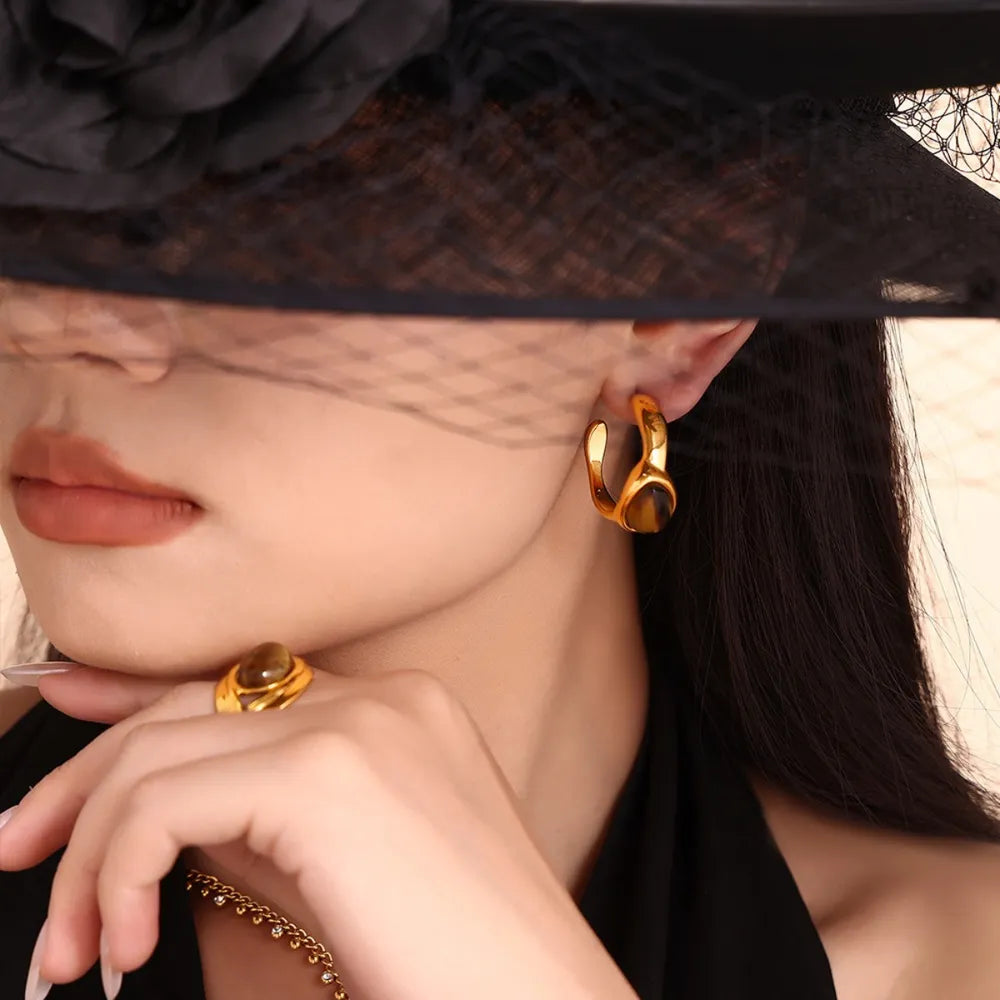 Gold sculptural hoop earrings with tiger's eye stone detail, shown on model.