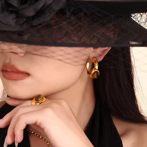 Gold sculptural hoop earrings with tiger's eye stone detail, shown on model.