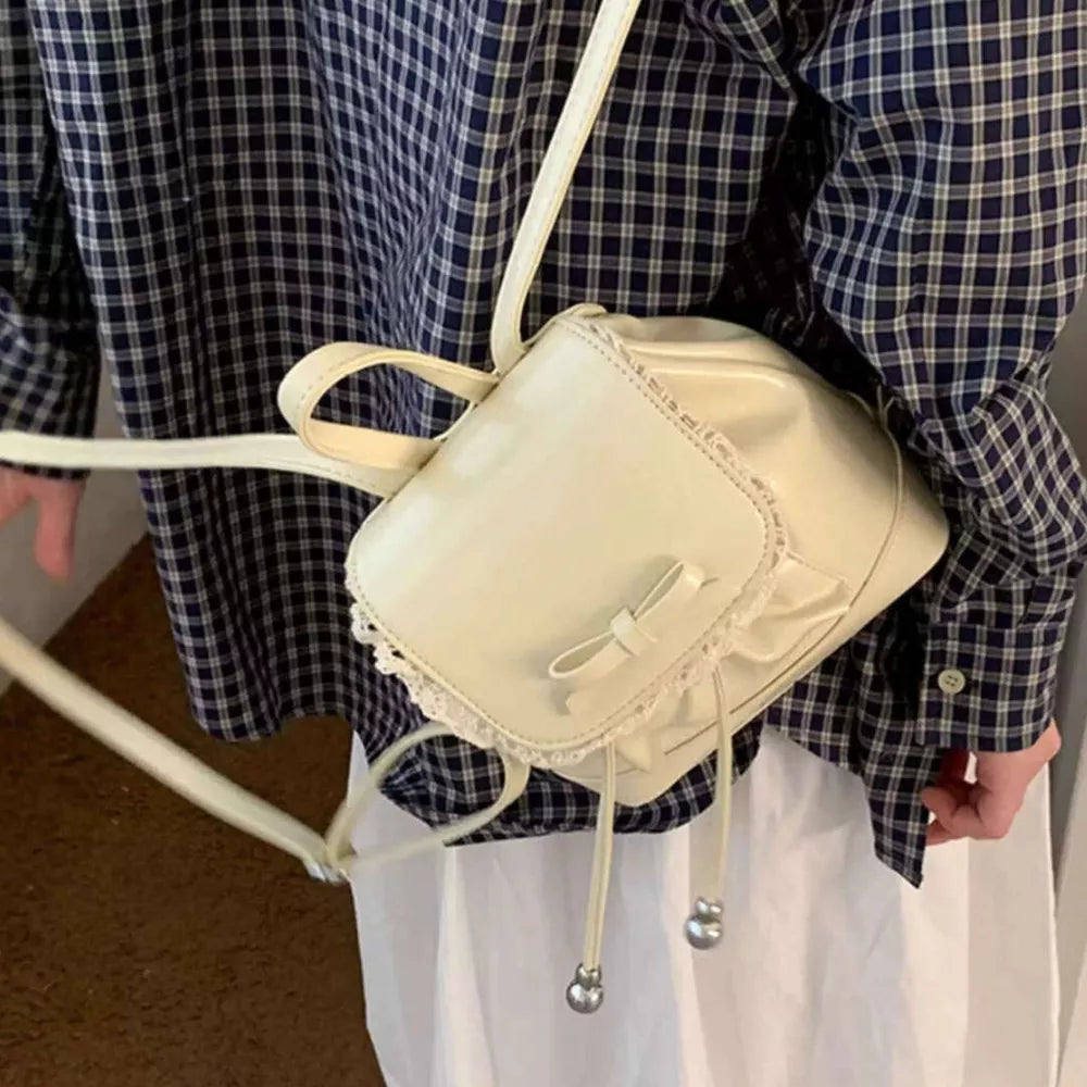 Cream mini backpack with lace trim and bowknot detail, silver hardware.