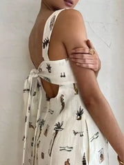 Sleeveless maxi dress in white with vacation-themed print, tie-back detail, and pockets.