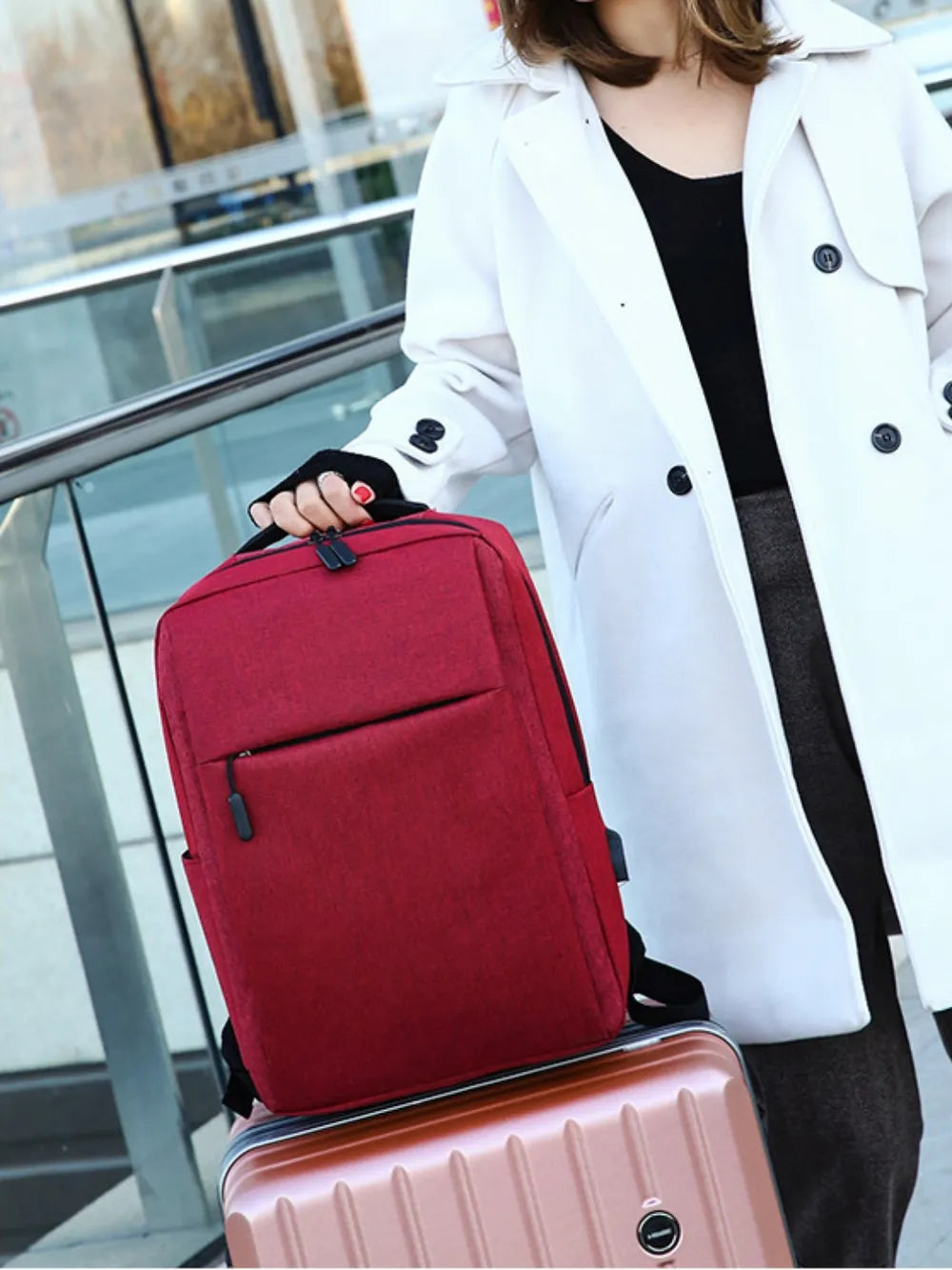 Burgundy canvas backpack with front zip pocket and side pocket, held by a person wearing a white coat.