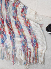 Textured knit hooded fringed cape in white with colorful diamond pattern and fringe detail.
