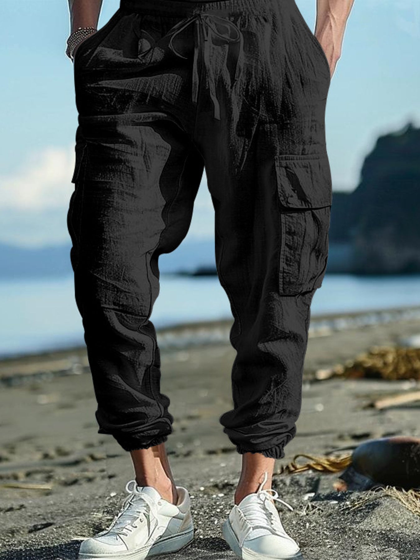 Black cargo pants with drawstring detail and elastic cuffs on a beach.