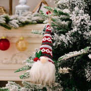 Gnome ornament with red and gray striped hat and white beard hanging on a flocked Christmas tree.
