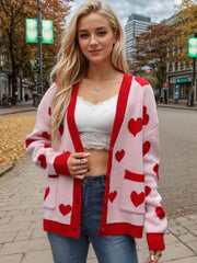 Blush pink acrylic cardigan with red heart intarsia pattern and red trim.
