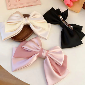Satin bow barrettes in blush pink, ivory, and black with alloy clips.